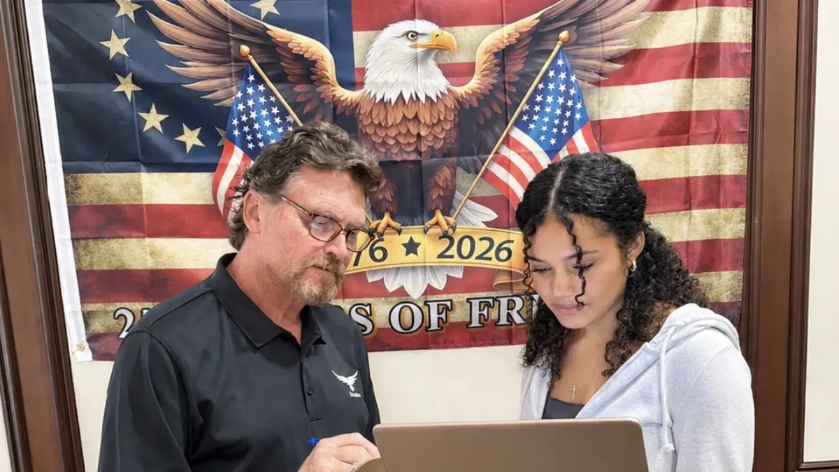 A Freedom Ave Maria teacher reviewing work with a student in front of an American eagle flag